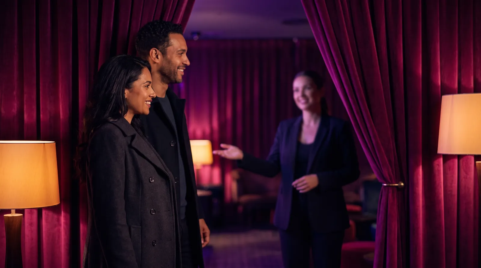 A couple are welcomed by a hostess at a velvet-curtained doorway